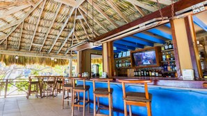 A bar area with wooden stools and a television screen.