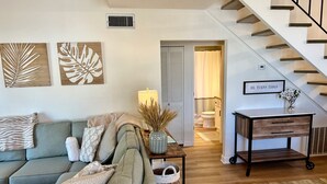 A living room with a sofa, a table with a lamp, and a staircase. - Flash Sale Completely updated 3/2 Sleeps 8 ML1 (Orange Beach)
