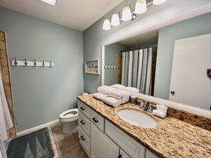 A bathroom with a granite countertop, a white sink, a mirror, a towel rack, and a toilet.