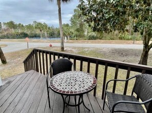A wooden deck with a round table and two chairs, overlooking a road and trees.