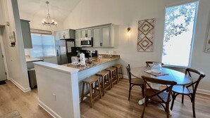 A modern kitchen with a central island, wooden bar stools, and a dining table with chairs. - Flash Sale Completely updated 3/2 Sleeps 8 ML1 (Orange Beach)