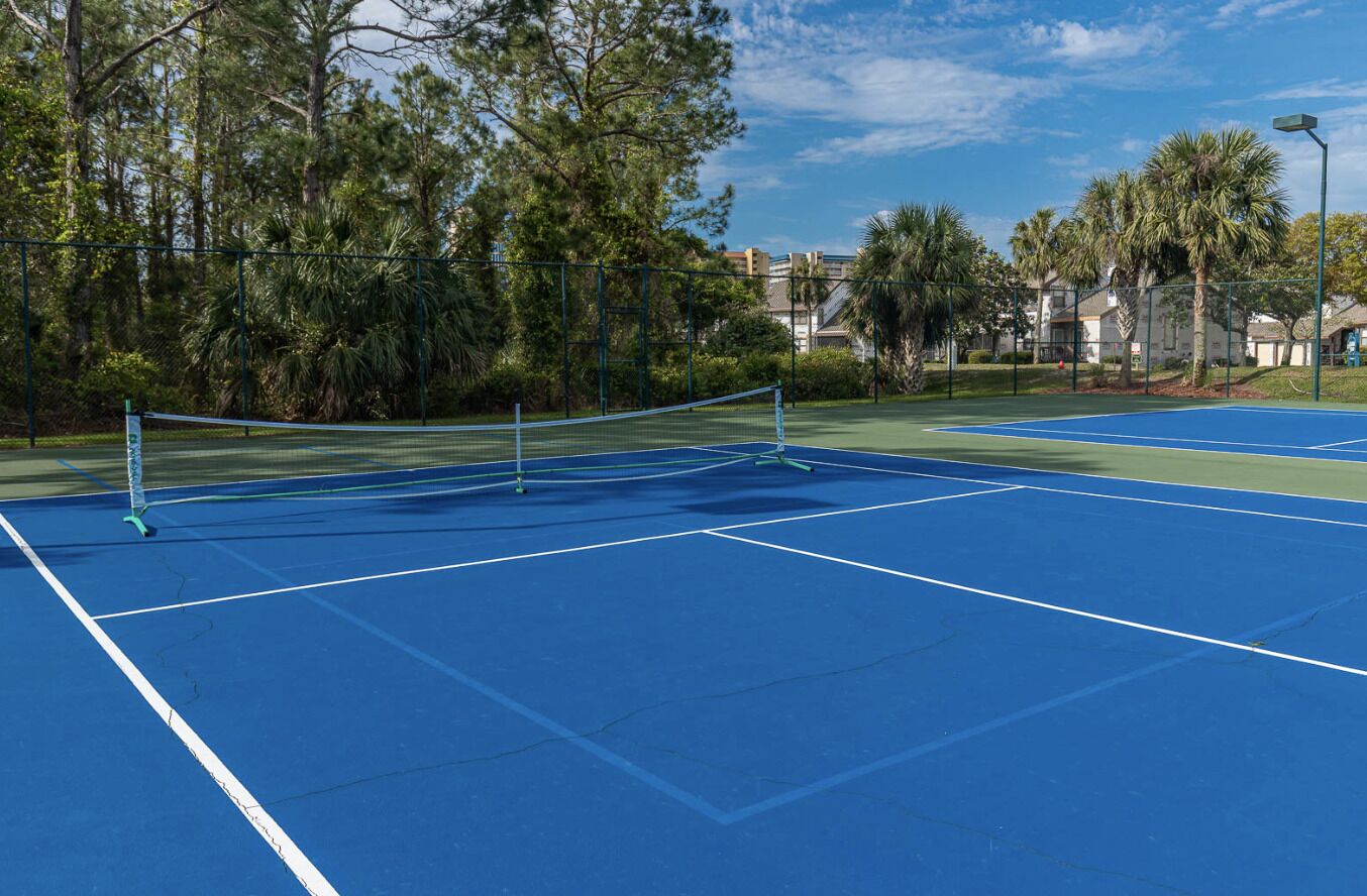 A tennis court with a net in the center, surrounded by trees and a fence.