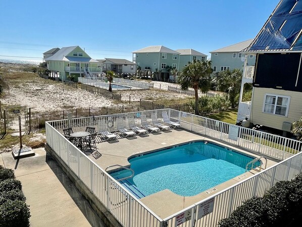 A swimming pool with a deck, surrounded by a fence, and houses in the background.