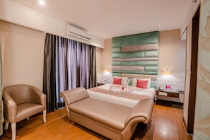 Habitación de hotel con una cama grande, un sofá, una silla, una mesita de noche y un aire acondicionado de pared.