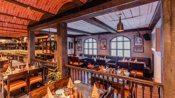 Un restaurante con mesas y sillas de madera, techo de ladrillo y amplios ventanales.