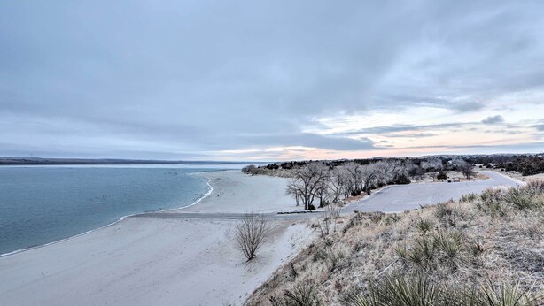 Ein Strand mit freiem Blick auf den Ozean, einem Parkplatz und einer Baumreihe.