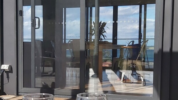 Una mesa con dos copas de vino y aperitivos en una terraza con vista al océano y un edificio moderno.