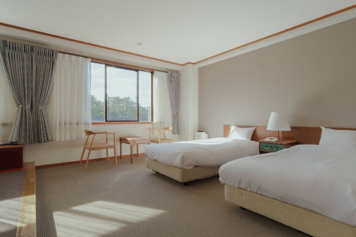 Een hotelkamer met twee bedden, een bureau, een stoel en een raam met gordijnen.