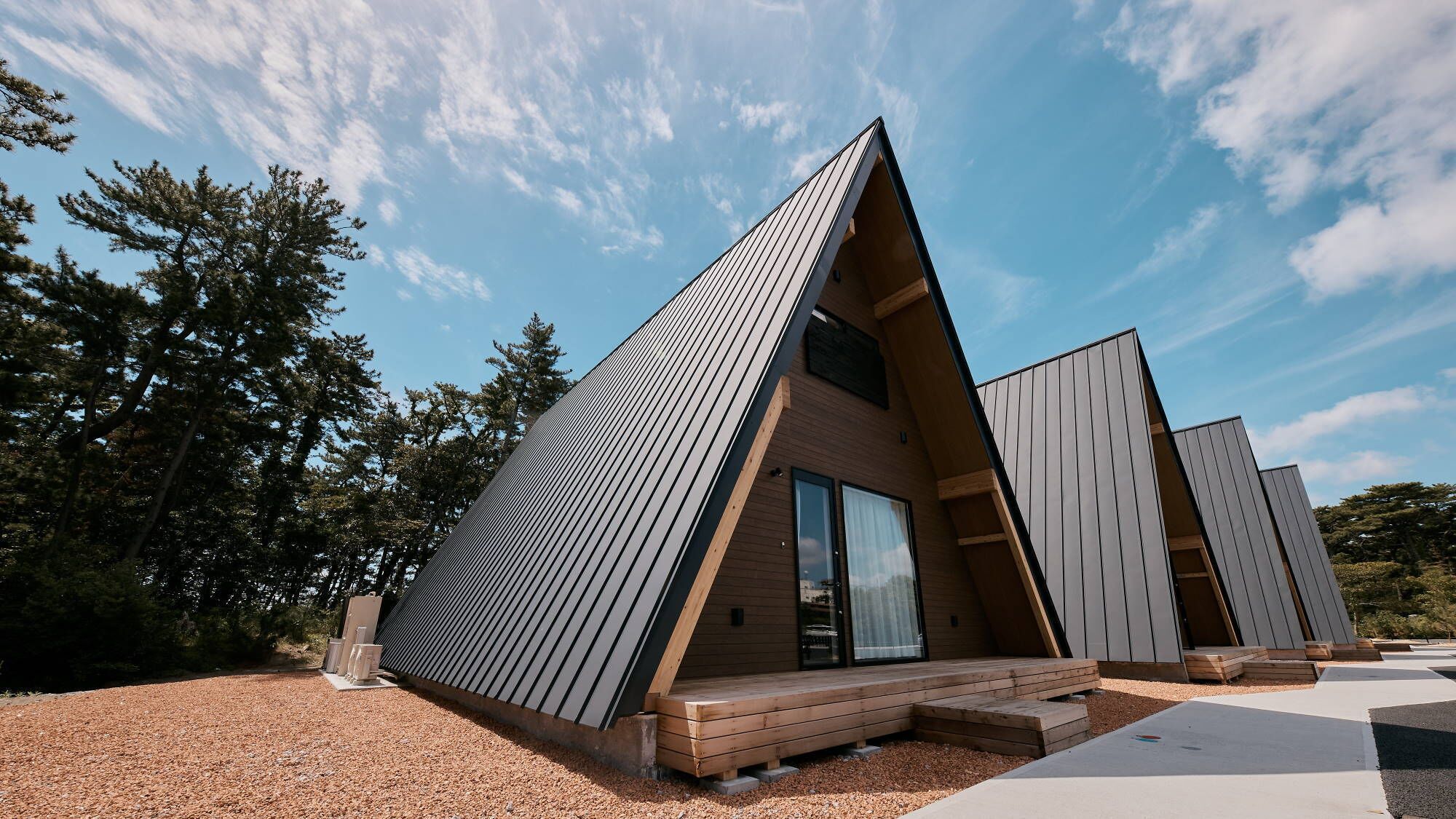Una estructura moderna en forma de A, tipo cabaña, con una terraza de madera y un amplio ventanal corredera.