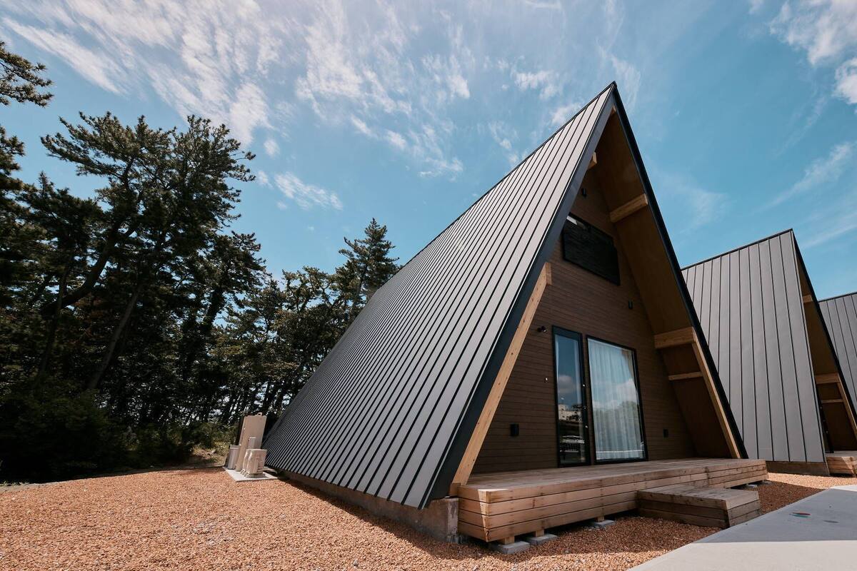 Een modern, driehoekig chalet met een houten terras en een grote schuifdeur van glas.