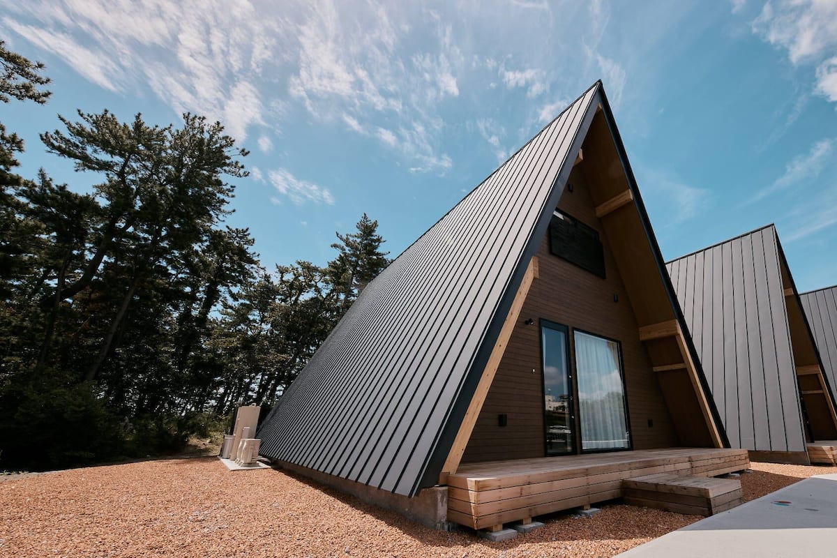 Una estructura moderna en forma de A, tipo cabaña, con una terraza de madera y un amplio ventanal corredera.