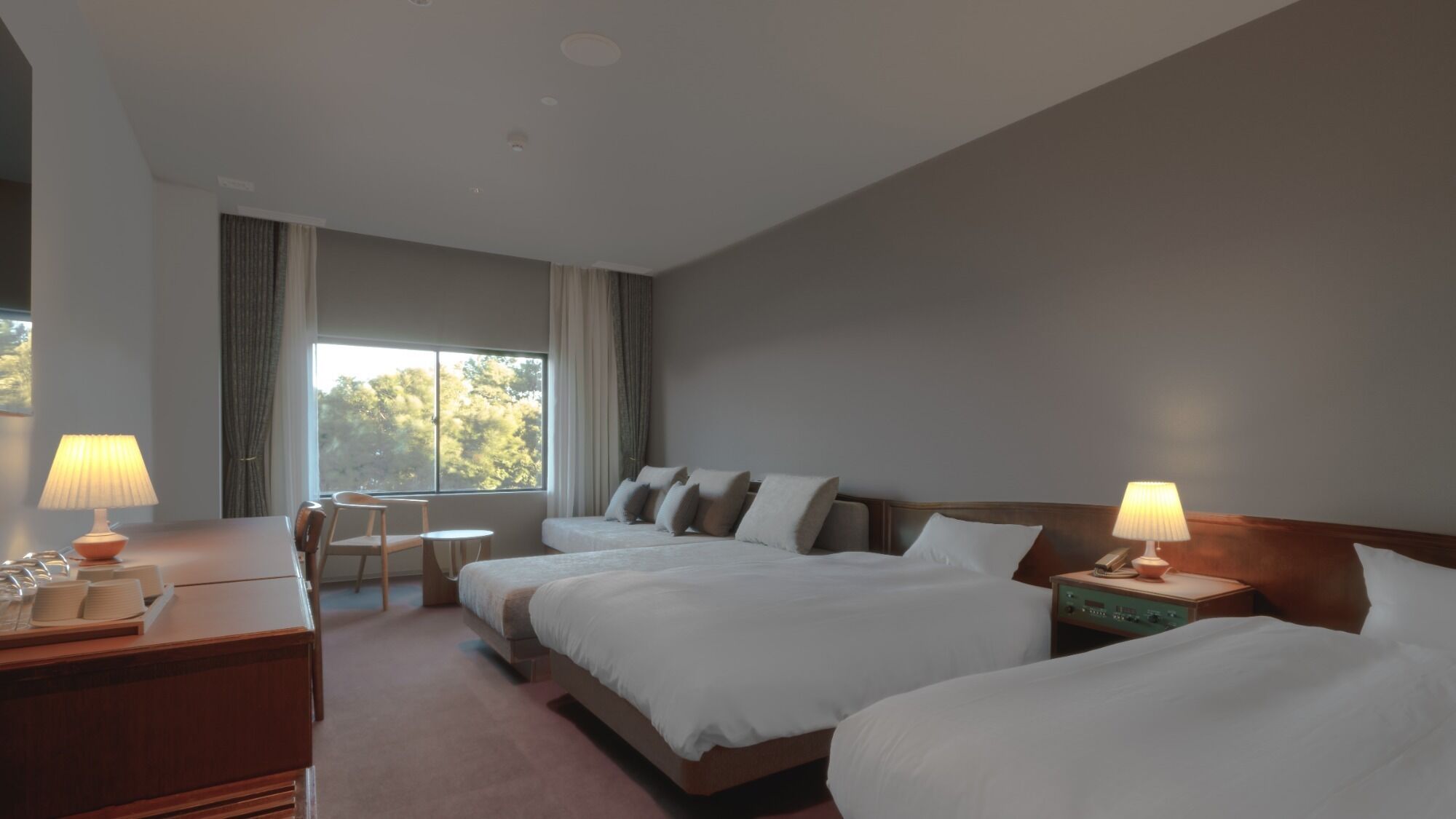 Habitación de hotel con dos camas, un escritorio, una silla, una mesita y una ventana con cortinas.