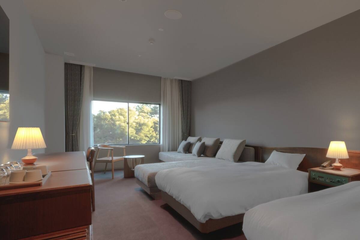 Een hotelkamer met twee bedden, een bureau, een stoel, een klein tafeltje en een raam met gordijnen.