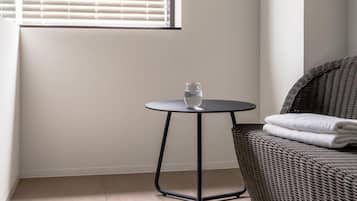 A room with a window, a round table with a glass, and a wicker chair.