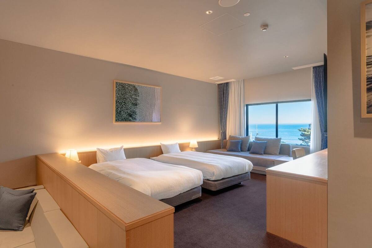 Een hotelkamer met twee bedden, een zithoek, een groot raam met uitzicht en een schilderij aan de muur.