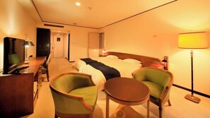 A hotel room with a bed, two armchairs, a small table, a desk with a TV, and a lamp. - Oarai Park Hotel (Oarai)