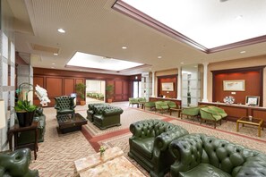 Un hall d’entrée spacieux, doté de canapés en cuir, de fauteuils verts, d’un comptoir d’accueil et d’une grande verrière.
