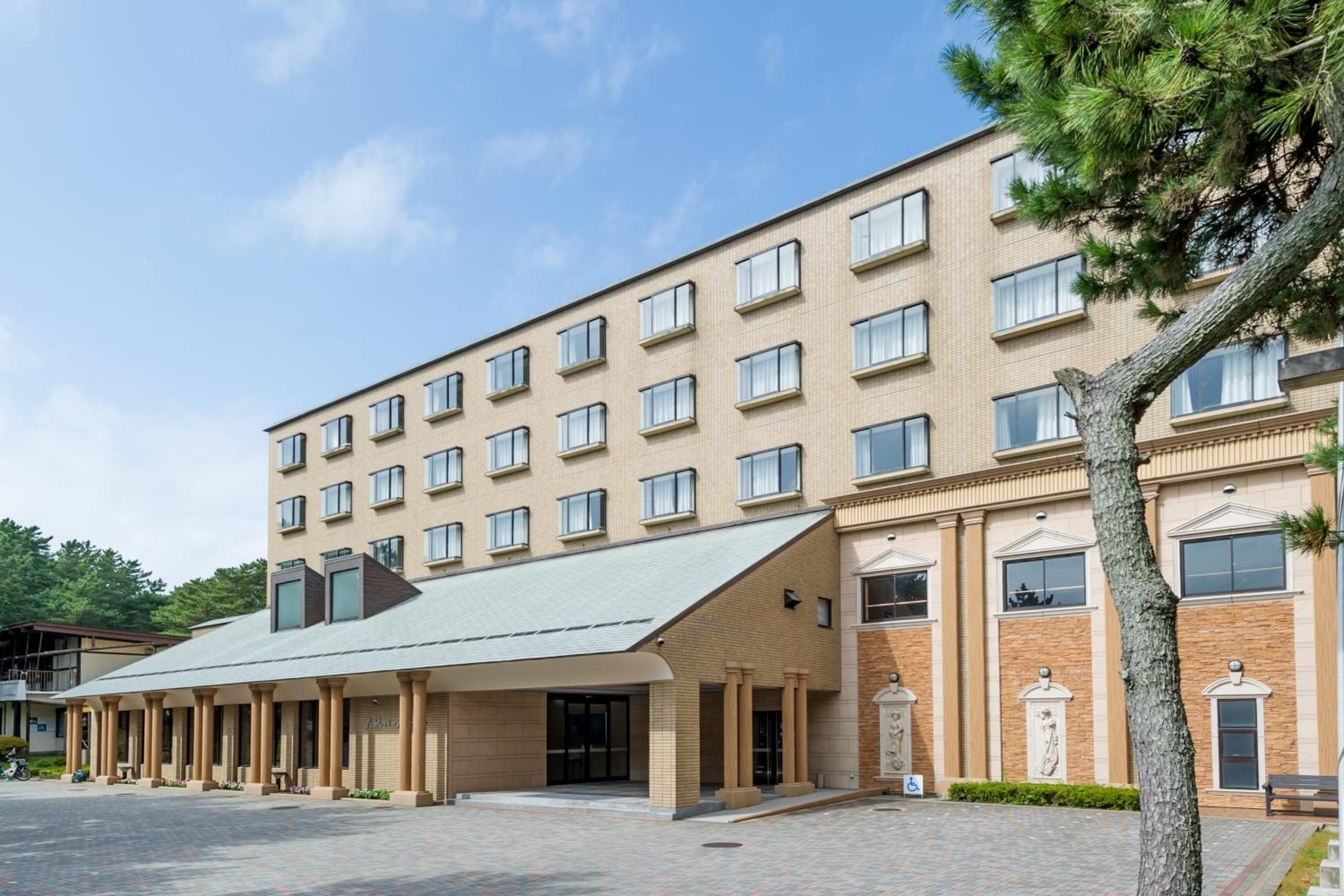 A multi-story hotel with a flat roof, large windows, and a central entrance with a covered walkway.