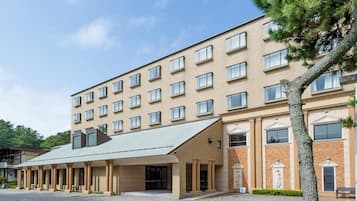 A multi-story hotel with a flat roof, large windows, and a central entrance with a covered walkway.