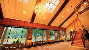Eine geräumige Lobby mit hoher Decke, großen Fenstern, einem Kronleuchter und einer Treppe.