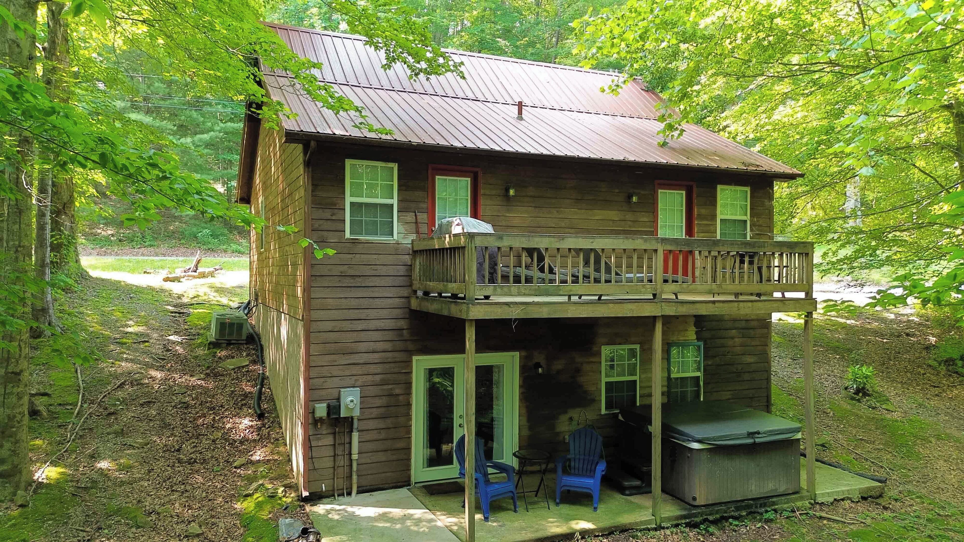 A two-story wooden cabin with a balcony, a covered porch, and a small outdoor seating area.