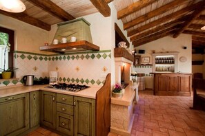 Enjoy cooking in this kitchen with a gas stove, coffee maker, and sink, adjacent to a bar area with wooden cabinets and a display of bottles.