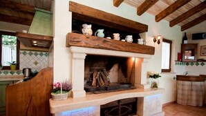 Eine rustikale Küche mit Kamin aus Stein, Holzbalken und einer gefliesten Spritzschutzwand.