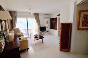 Habitación de hotel con sofá, mesa de centro, televisión, puerta de madera y ventana con cortinas.