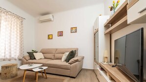 A living room with a beige sofa, a white coffee table, a flat-screen TV, and a small side table with lamps. - Apartment Family Tokić  (Dubrovnik)