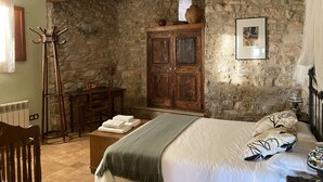 Une pièce rustique avec un mur en pierre, des meubles en bois, un lit avec des oreillers et un porte-manteau.