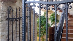 Un portail en fer forgé, orné de barreaux verticaux et d’éléments décoratifs, qui mène à un mur en pierre et à un escalier.