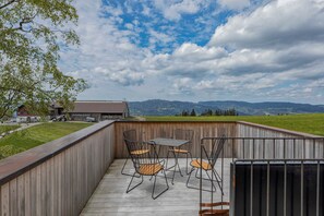 A wooden deck with outdoor seating, a view of a farm, and distant mountains. - Adventure tree house, Baldauf family - Tree house (Sulzberg)