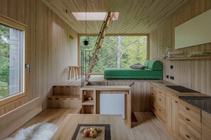 A compact, modern kitchen with wooden cabinetry, a dining area, and a staircase leading to a loft bed.