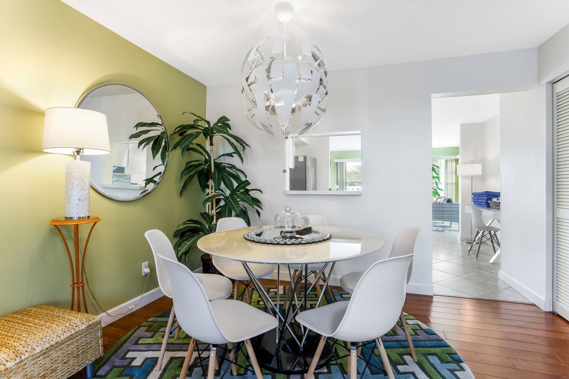 Un coin repas avec une table ronde, des chaises blanches, un lustre et un grand miroir au mur.