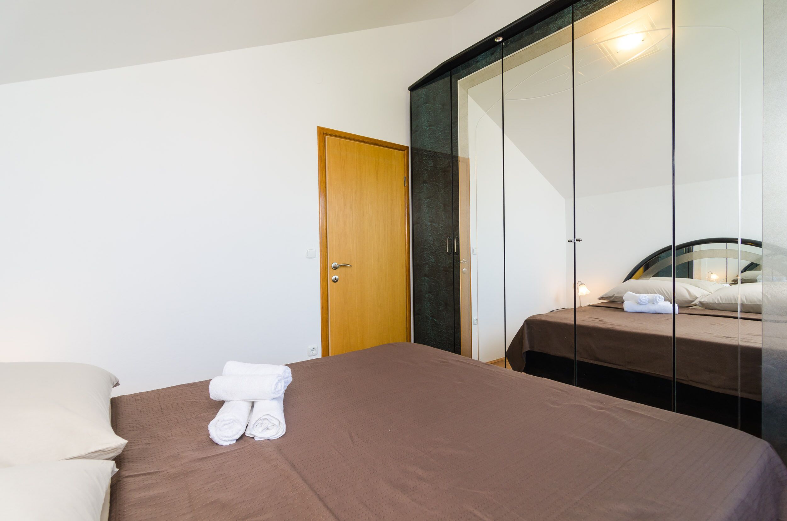 A hotel room with a bed, a wooden door, and a wardrobe with a mirror.