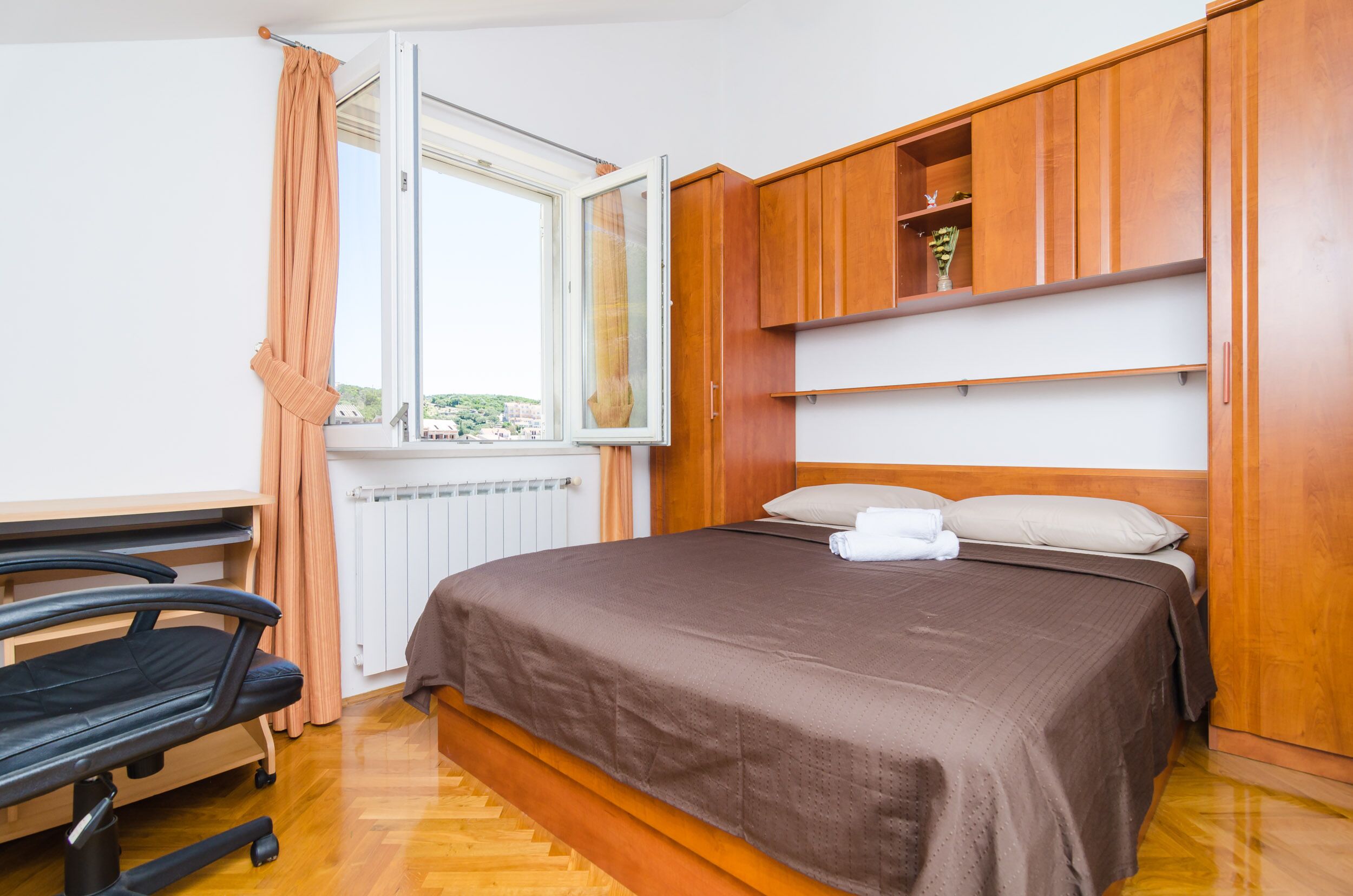 Une chambre à coucher comprenant un lit, une armoire en bois, un bureau avec une chaise et une fenêtre avec des rideaux.