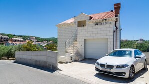 En vit BMW stod parkerad framför en byggnad med ett tak täckt av takpannor och en trappa som ledde ner till ett garage.