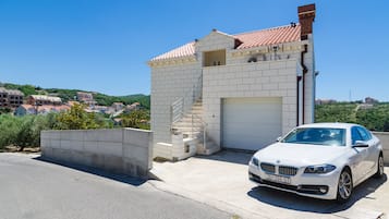 Un BMW blanco estacionado frente a un edificio con techo de tejas y una escalera que lleva a un garaje.