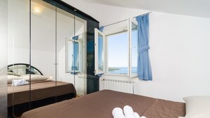 Ett hotellrum med en säng, en extra säng, ett stort fönster med gardiner och utsikt över havet.