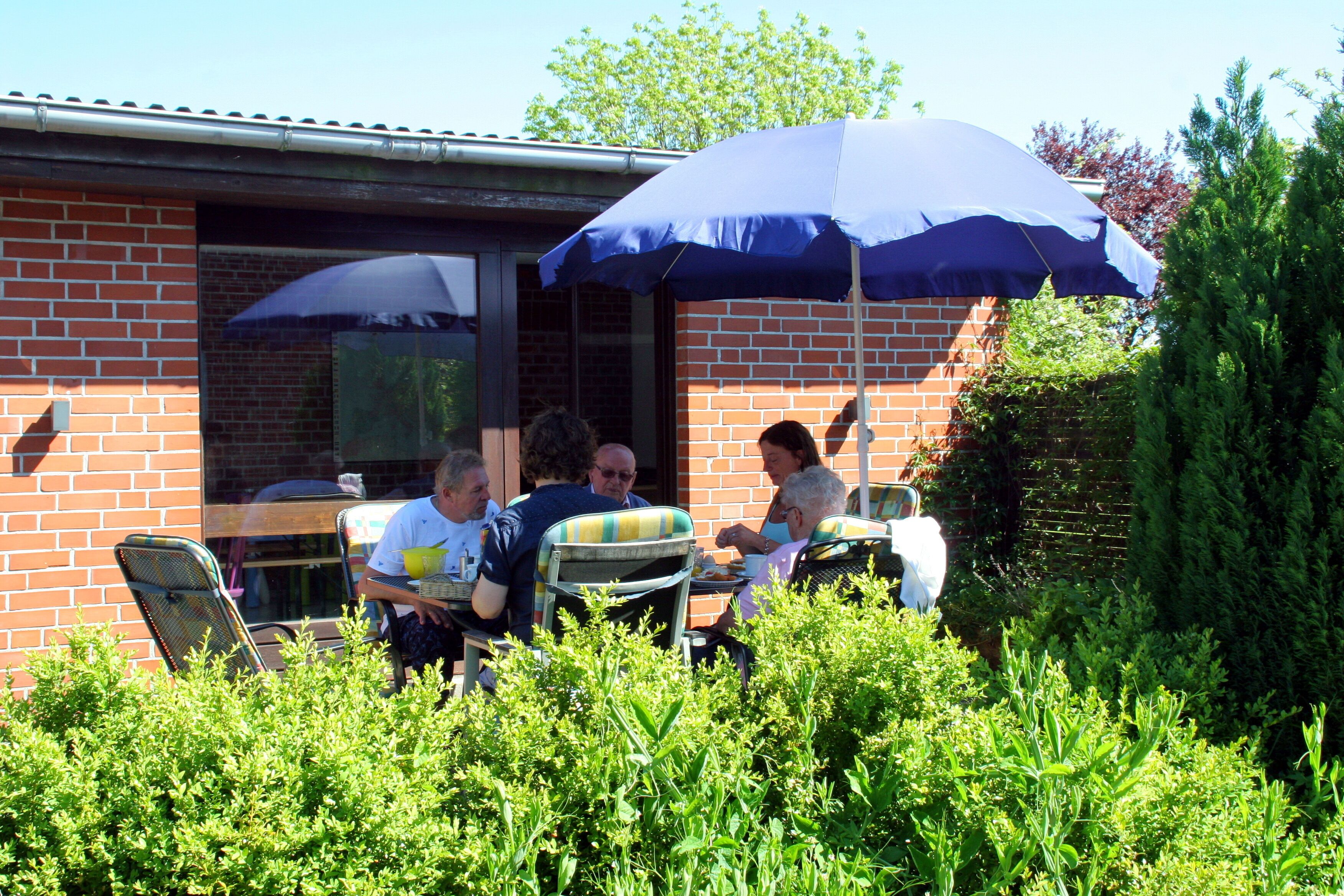 Une terrasse extérieure avec des murs en briques, des chaises en métal et un grand parasol bleu qui offre de l’ombre.