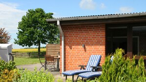 A brick building with a covered patio area, two striped lounge chairs, and a wooden table. - Baltic Sea vacation in an old granary (Heringsdorf)