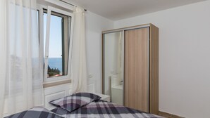 A bedroom with a bed, a window with curtains, a wardrobe, and a view of the sea. - Apartment Med (Dubrovnik)