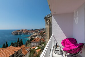Uma varanda com vista para uma cidade costeira, uma mesa com uma cadeira e uma bandeira.