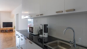 A modern kitchen with white cabinets, a black countertop, a stainless steel sink, a microwave, and a coffee maker. - Apartment Med (Dubrovnik)