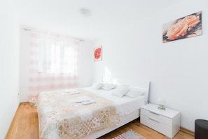 A bedroom with a bed, a nightstand, a lamp, and a painting of roses. - Apartment Budimir (Supetar)