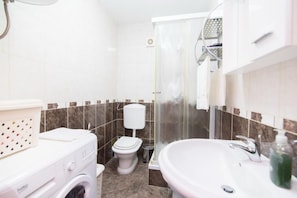 A bathroom with a washing machine, toilet, shower, and sink. - Apartment Budimir (Supetar)