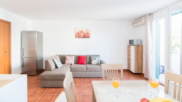 A modern living room with a sofa, a dining table with fruit and drinks, a refrigerator, and a cityscape painting. - Apartment Budimir (Supetar)