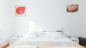 A neatly made bed with white linens, a floral-patterned bedspread, and two wall-mounted paintings of flowers. - Apartment Budimir (Supetar)