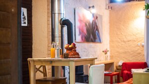 Un interior rústico con una mesa de madera dispuesta con fruteros, botellas y vasos. Se ven una silla roja y un sofá al fondo.