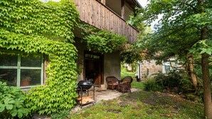 Una casa con muros cubiertos de hiedra, un balcón de madera y un jardín con mobiliario exterior.